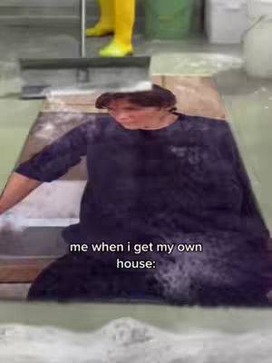 The image shows a person, possibly the creator, in a room with a mopping tool. Text overlays read 'me when i get my own house:'. The person is in the foreground, while the background has another person wearing yellow clothing and green buckets.
