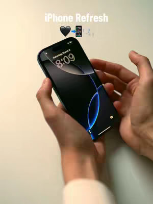 A person's hands holding a dark-screened iPhone, with text overlayed. The phone displays a dark background with a blue gradient around the edges and showing time. The background is mainly white. Overlay text reads 'iPhone Refresh' with a heart and a phone icon.