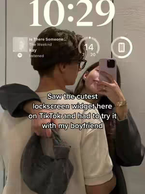 A couple is embracing while looking at a phone displaying a lock screen with a widget. The text overlay is in a white, blocky font.