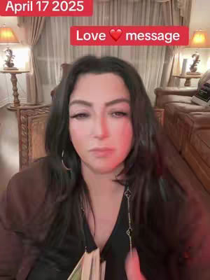 A woman with long black hair is looking at the camera with a neutral expression. There are two text boxes at the top that read 'April 17 2025' and 'Love message'.  She is wearing a dark top with a silver colored necklace and a jacket and is in front of a background of a room with curtains, two lamps, and some wooden furniture. The lighting is soft.