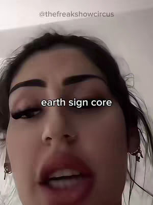 A close-up shot of a woman's face, with her head filling most of the frame. She has dark hair, and her eyebrows are sharply defined. Her eyes are slightly open, and her lips are parted as if she's speaking. The text on the image says "earth sign core".