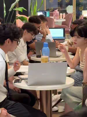 A cover image showing a group of people, possibly in a cafe or office setting, gathered around tables and laptops. Several people are in focus, some looking at laptops, others engaged in conversation. The environment is casual, with laptops and drinks on the tables. Colors are warm, with indoor lighting.