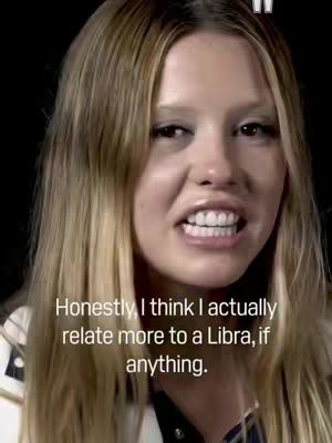 A close-up shot features a woman with long, light blonde hair against a dark background. She is looking directly at the camera with a slight frown and slightly parted lips, revealing her teeth. Text overlayed on the image indicates she is discussing her astrological sign.