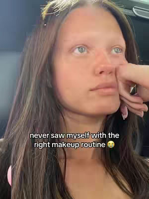 A selfie-style shot of a woman with brown hair looking towards the upper right. She has fair skin and appears to be in the middle of, or just before, applying makeup. The text overlay reads, 'never saw myself with the right makeup routine'