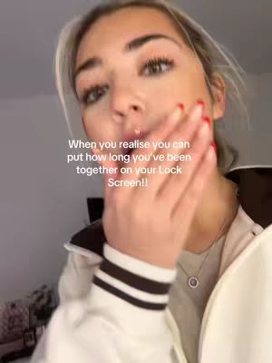 A young woman with blonde hair and red nail polish is shown in a close-up shot. She is holding her hand up to her face, covering her mouth slightly, while looking towards the camera. Text is overlaid on the image.