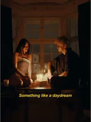 An indoor scene at nighttime, with a woman and a man sitting opposite each other by the window. They are in semi-darkness, with a warm, candlelit ambiance illuminating their faces and the objects between them. In the center, there's a cake with candles, and the scene conveys a sense of intimacy and nostalgia. The background shows a window with the outside world visible through it.