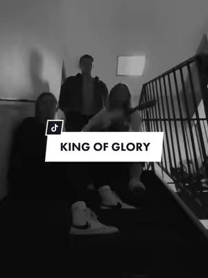 A black and white image shows three people standing on a staircase. The person in the middle is slightly taller than the others, with the ones on the side being partially obscured by the darkness. A white rectangular overlay with the text "KING OF GLORY" in all caps appears on the bottom of the image.