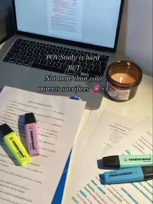 A well-lit desk with documents, highlighters, and a laptop. In the background, a lit candle adds warmth. The composition creates a focused study setting.