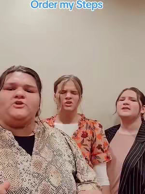 The cover image features three young women singing, captured from the chest up. The woman on the left is in the foreground and has tan skin, her facial expression appears open, and she is wearing a patterned jacket over a black top; also, she has a neutral expression. The woman at the center is lighter-skinned with long, light-colored hair; they are wearing an orange floral top, and a white layer is peeking through. On the right is the third woman, also lighter-skinned, with a neutral expression wearing a pink top and a black blazer. The background is a simple cream-colored wall. The video's hook is displayed at the top in white text on a blue rectangular text box.