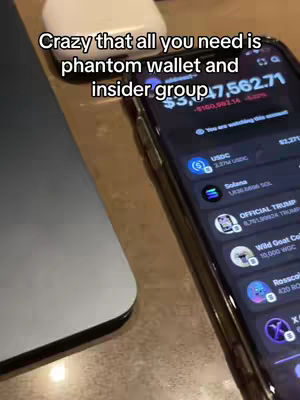 The cover image captures a close-up view of a smartphone displaying a cryptocurrency wallet interface. The phone rests on a wooden surface next to a partially visible laptop and a white charging case. The screen shows financial data, including a balance of $17,562, and various cryptocurrency listings like USDC and Solana, with the screen's dark interface providing a contrast to the surroundings. Text overlays describe the content.