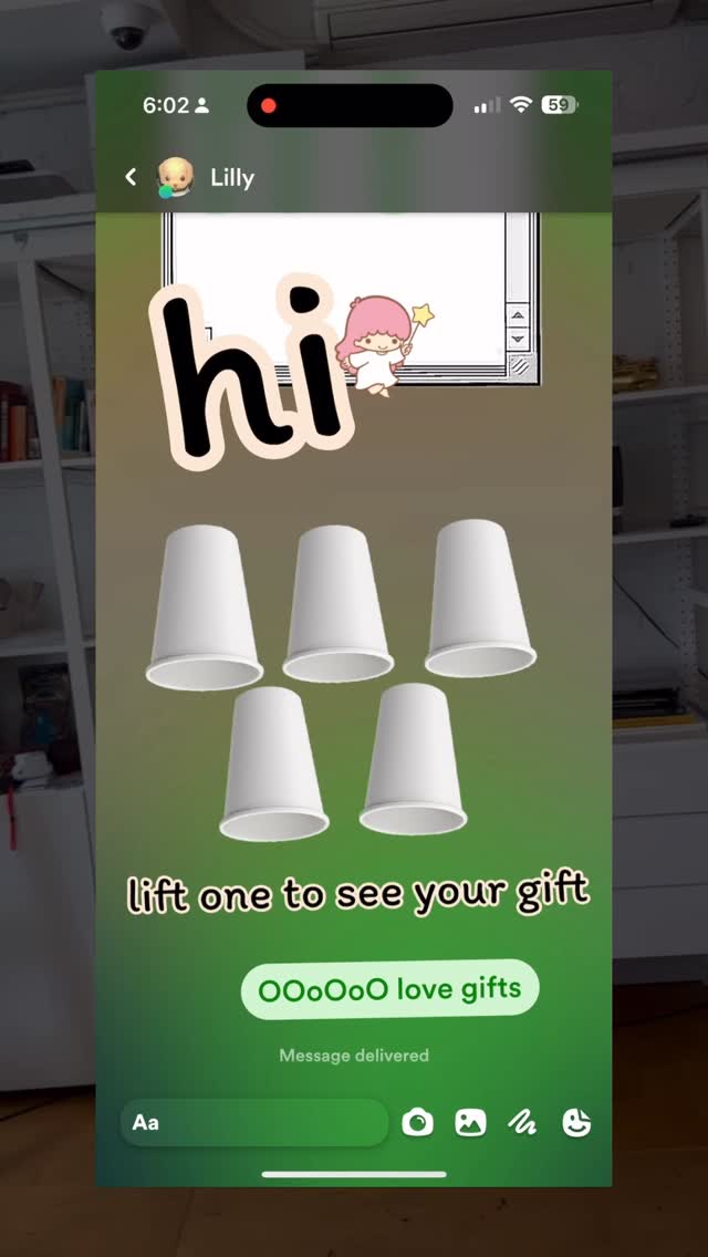 A phone screen displaying a chat interface. The background is green, it has a chat with a user called Lilly. There are five white cups presented, and the text overlay says 'lift one to see your gift'. Below, there is the message ' Message delivered'.