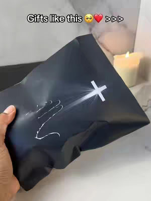 A hand holds a black gift bag with a white cross design, against a background with a lit candle and a blurred backdrop. The hook reads "Gifts like this".