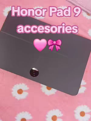 A top-down shot of a dark tablet lying on a pink surface decorated with white daisy patterns. Above the tablet are the words "Honor Pad 9" in a pink, bold font, followed by "accesorios" in a similar style. A pink heart emoji and a pink bow emoji are placed next to the word accessories.