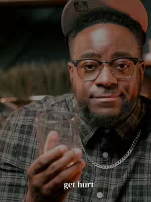 A man with a beard wearing glasses and a cap, holding up a glass. Text overlayed on the bottom.