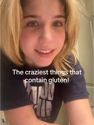 A close-up shot of a blonde woman with fair skin, smiling slightly. She's wearing a dark blue t-shirt with text on it. The overlay text reads "The craziest things that contain gluten!"
