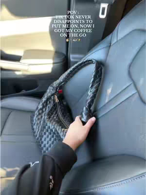 A hand holding a woven black bag in a car. The image is taken from a first-person perspective from inside the car.