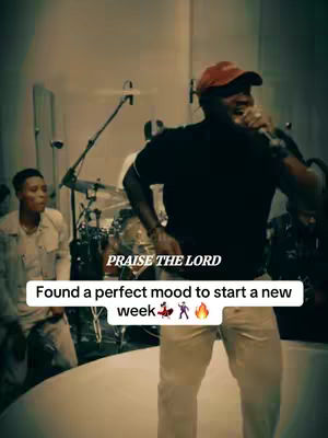 A man in a red cap, black shirt, and light pants is singing into a microphone on a stage. Behind him is a band, with a drummer and other musicians partially visible. The stage is lit with soft lighting. The image has text overlays including "PRAISE THE LORD" and "Found a perfect mood to start a new week" in a white box. The overall composition of the image is a medium shot.
