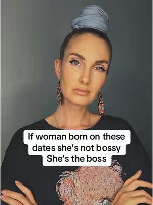 A woman with fair skin and light makeup is the central focus, her gaze directed towards the viewer. She has an updo hairstyle and is wearing sizable earrings. The background is a plain, neutral gray. A text overlay at the bottom of the frame declares, \"If a woman born on these dates she's not bossy, she's the boss.\"