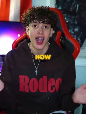 A young man with curly hair is the central focus, looking directly at the camera with an open mouth. He is wearing a dark hoodie with the word "Rodeo" in large red letters. A silver chain with a cross pendant hangs around his neck. The background fades, but includes an American flag and a red gaming chair.