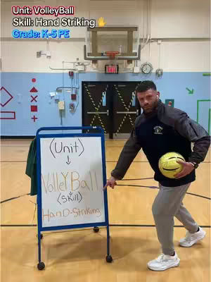 A man in athletic attire poses in a gymnasium with a volleyball, pointing at a whiteboard that reads "VolleyBall (Skill) Hand Striking". The image has a bright, well-lit indoor setting.