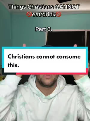 A man in a white hoodie with green accents holds his hands up, with a blue and white text overlay covering his face. The background shows a light blue wall and some dark objects.