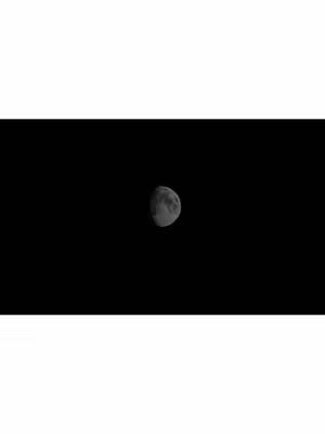 The image is a high-contrast monochrome composition. The top portion is bright white while the bottom is completely black, and in the center of the dark area is a crescent moon, which is slightly overexposed making its features still visible. Overall, it creates a stark contrast between the moon and the space in front of it.