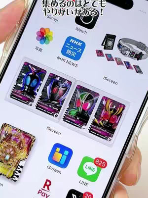 A screenshot of a smartphone screen displaying a custom home screen theme featuring images and icons from the Kamen Rider franchise. The phone is held at an angle, with the screen showing various app icons, Kamen Rider themed card images, and other widgets. The background appears to be a light-colored surface. Text is overlaid on screen in Japanese.