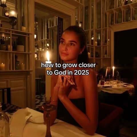 A woman sits at a candlelit table in a restaurant, looking upwards with a thoughtful expression. The image is warmly lit, with the woman's face illuminated by candlelight. The text overlay reads 'how to grow closer to God in 2025'.