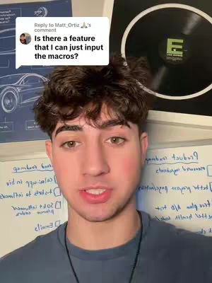 A young man with short, dark hair and brown eyes is centered in the frame, looking at the camera and speaking. He's wearing a dark blue t-shirt, and a necklace is visible. The background is a mix of whiteboards with handwritten notes and charts, along with a blue poster. In the top right corner, a black vinyl record with a white label featuring the letter 'E' in a green circle is visible.