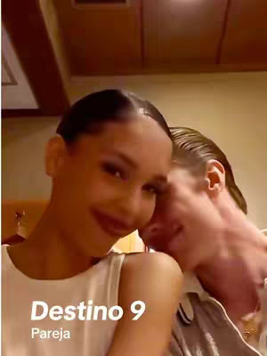 The cover image is a medium shot of two people close together. The person on the left has dark hair pulled back and is smiling, wearing a white top. The person on the right has light hair and is leaning in with their face near the other person's. The background is a warm, neutral tone. Text overlay at the bottom lists 'Destino 9' and 'Pareja'.