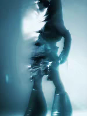 An out-of-focus, abstract image dominated by cool blues and silvers. The distorted figure of a person is suggested, likely a fluid dancer or model with undefined features, rendered with blurred edges to create an ethereal effect. The lighting is soft and uniform, providing a sleek, modern aesthetic.