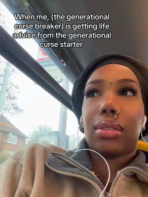 A close-up shot of a woman's face, framed from the chest up, looking out the window of a moving vehicle. She has dark skin, a dark head covering, and is wearing earbuds. The background outside the window shows houses and trees, suggesting a suburban or residential area. The color palette is natural, with a mix of outdoor light and vehicle interior.