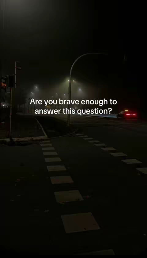 A nighttime street scene with a dark, moody atmosphere. The road is wet, and a few streetlights illuminate the scene. Fog obscures the background. Text overlayed on the image.