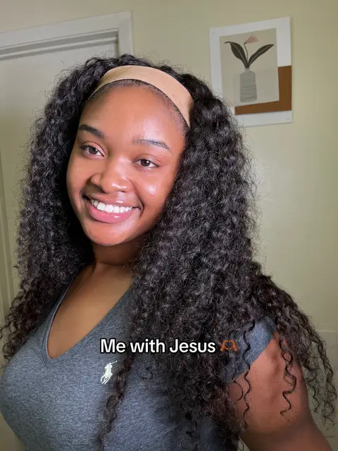 A smiling woman with long, curly black hair and a brown headband looks directly at the camera. Text in a white box at the bottom of the image reads, 'Me with Jesus'. The background includes a plain wall, a painting, and a glimpse of a mirror.