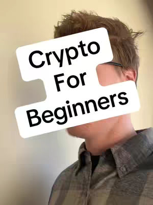 A man's face is partially obscured by a white overlaid shape containing bold black text. The man has short, light brown hair and neutral skin tone. The text reads 'Crypto For Beginners'. He is wearing glasses and a plaid shirt, and the background is a plain light wall.