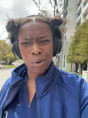 A woman with two buns and headphones is walking in front of a building, looking at the camera with a questioning expression. The caption includes the word "Sagittarius."