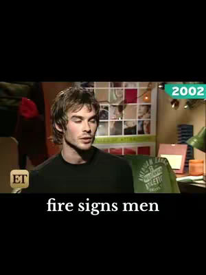 A man with brown hair is centered in a medium-shot of the video frame. The backdrop features a cluttered area with posters, a desk, and a green item with white text. Overlayed at the bottom is the text 'fire signs men' in a white, bold font. The video is shot in a dimly lit room.