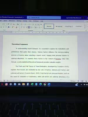 A laptop screen displaying a Microsoft Word document titled "Theoretical Framework." The text is legible, and the background shows a desk environment. The layout is typical of a research paper or academic document.