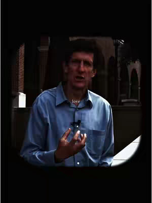 A man in a blue shirt is speaking. The word 'love' is overlaid in white at the center of the image.