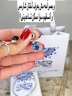 A woman's hand holding a turquoise charm bracelet component with a white and blue patterned bag and other jewelry visible in the background. The woman has vibrant red nail polish. Text is overlaid at the top.