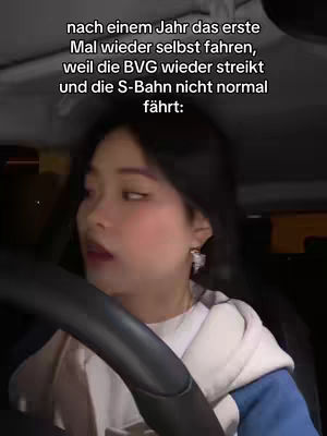 A young woman is filmed from the chest up, seated in what appears to be a car. She's gazing slightly off to her left, with a somewhat surprised or concerned expression. The interior is dim, with the steering wheel visible, and text overlays are positioned at the top.