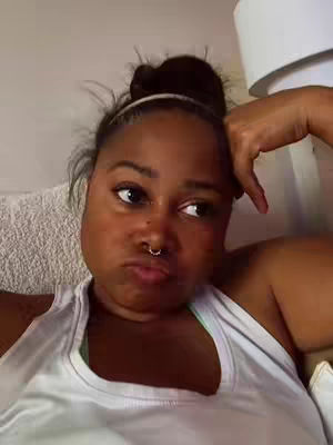 The cover image shows a close-up of a Black woman with a raised bun hairstyle, wearing a white tank top. She has a nose ring and a slight pout. One hand is on her face, and her gaze is directed to the side. The background is blurred.