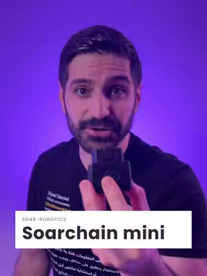 A man with a beard and short dark hair is holding a small black device in front of a vibrant purple background. He has a focused expression and is looking directly at the viewer. A white bar with the text 'Soarchain mini' is placed at the bottom of the image.