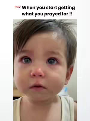 A close-up shot features a light-skinned baby with short, dark hair and tear-filled eyes that appear blue-grey. The baby's face is the central focus, with cheeks slightly flushed and a small, open mouth. The baby is wearing a cream-colored tank top, and a thin, white border surrounds the image. Above the baby is the text overlay in red color.