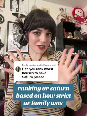 A woman with dark hair and bangs is centered in the frame, gesturing with her hands. She's wearing a striped shirt, and a message overlayed on the image asks viewers to rank Saturn placements based on family strictness. Behind her is a room with framed art and collectibles.