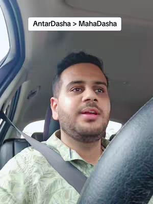 A man is driving a car, seen from his perspective. A text overlay at the top says, "AntarDasha > MahaDasha". The scene primarily features the driver's face, parts of the steering wheel, and the car's interior.
