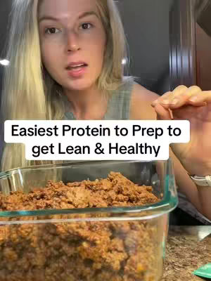 A woman is shown in a kitchen setting, looking toward the camera and smiling with a contained meal prep container in the foreground. The container is filled with a ground meat mixture. A text overlay at the bottom indicates the video's message about easy protein preparation.
