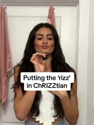 A woman in a white top is holding a small black container. She's in front of a white door with a pink item hanging on it. The text overlay reads, "Putting the 'rizz' in ChRIZZtian".