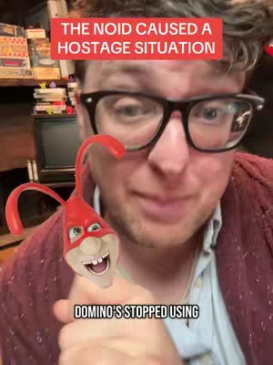 A close-up shot features a man with glasses in the foreground with a red text box above his head and animated character overlaid on his lower face. Background details include shelves with various items.