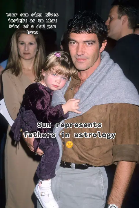 The image features a man, presumably Antonio Banderas, holding a young girl. Text overlays state the video's theme about sun signs related to fathers in astrology. The man is wearing a brown shirt and grey pants and has a light grey sweater draped over his shoulders. The little girl, wearing a burgundy dress, rests her head on his arm. The background shows another woman and some other people.